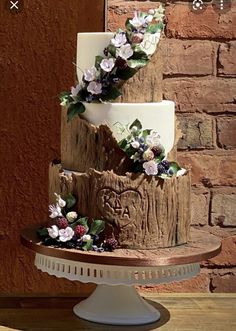 a three tiered cake decorated with flowers and greenery on a wooden table in front of a brick wall