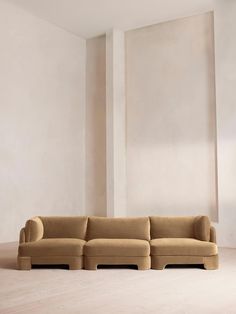 a beige couch sitting in the middle of a living room next to a white wall