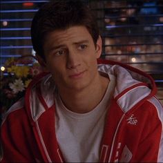 a young man in a red and white hoodie looks at the camera while sitting down