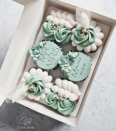 four decorated cupcakes in a box on a table with white and blue decorations