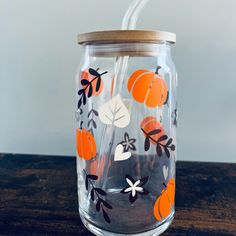 a glass jar with oranges and leaves painted on the inside is sitting on a wooden table