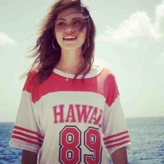 a woman standing in front of the ocean wearing a shirt that says hawaii 89 on it