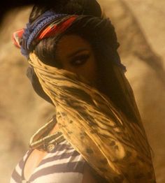 a woman in striped shirt and head scarf next to large rock