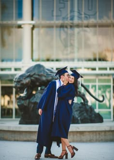 a man and woman hugging each other in front of a building wearing graduation gowns