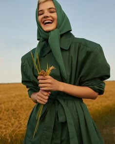 a woman in a green raincoat smiles while standing in a field with tall grass