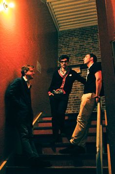 three men are standing on the stairs and one is holding his hand out to another man