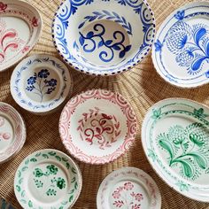 many different colored plates sitting on top of a wicker tablecloth with designs painted on them