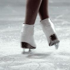 the legs and feet of a person wearing ice skates on an icy surface with snow flakes