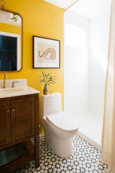 a white toilet sitting next to a sink in a bathroom under a mirror and framed pictures on the wall