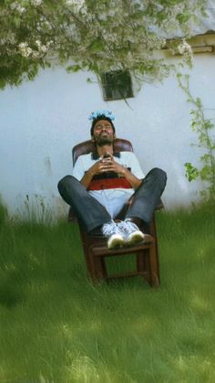 a man sitting on top of a wooden chair in the grass