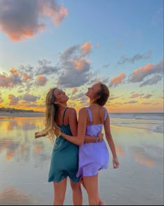 two women are standing on the beach and smiling at each other as the sun sets