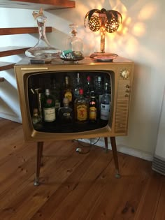 an old fashioned television with liquor bottles on it's side table next to a lamp