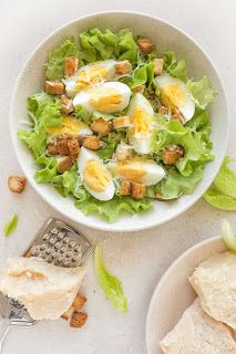 a white bowl filled with lettuce and hard boiled eggs next to crackers