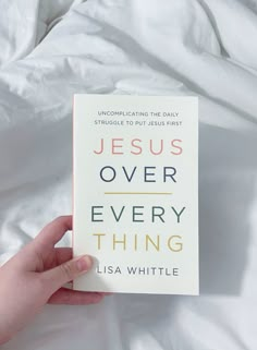 a person holding up a book on top of a white bed covered in sheeting