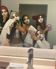 four women with white face paint on their faces are taking a selfie in the mirror