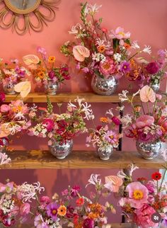 a bunch of vases filled with flowers on top of a wooden shelf in front of a pink wall