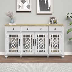 a white sideboard with glass doors and two pictures on the wall