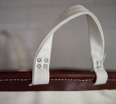 a close up of a white bag on a brown leather handle with two silver beads