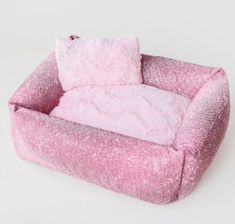 a pink dog bed with a fluffy pillow on it's back and two pillows in the middle