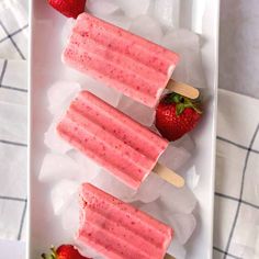 three popsicles with strawberries on them sitting on ice in a white tray next to two forks