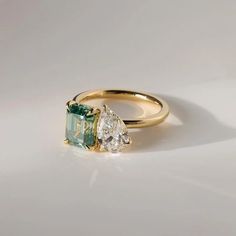 an emerald and diamond engagement ring on a white surface with the light reflecting off it's side