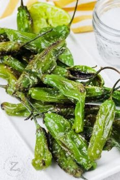 some green peppers on a white plate next to a jar