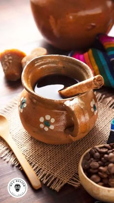 there is a cup of coffee and spoons on the table next to some beans