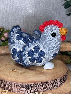 a crocheted chicken sitting on top of a piece of wood next to flowers