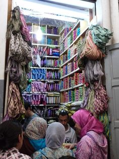 a group of people standing in front of a store filled with different types of scarves