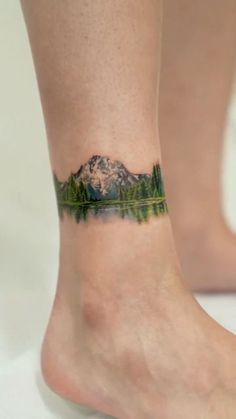 a woman's foot with a mountain and trees tattoo on the side of her leg