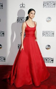 a woman in a red dress posing on the red carpet at an awards event with her hands in her pockets