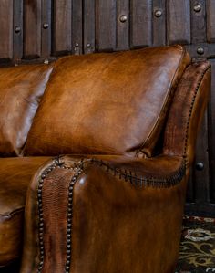 a brown leather couch sitting in front of a wooden paneled wall with studded trim