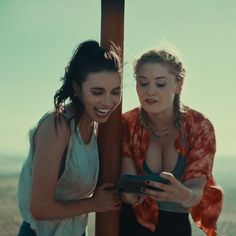 two women standing next to each other looking at a cell phone