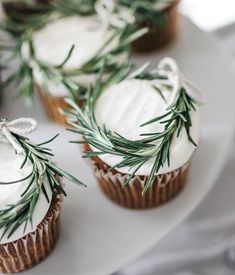 some cupcakes with white frosting and green sprigs on top are sitting on a plate