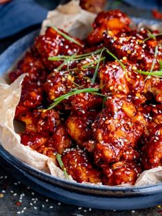 a blue bowl filled with meat covered in sauce and garnished with green onions