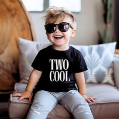 a little boy sitting on top of a couch wearing sunglasses with the words two cool printed on it