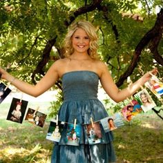 a woman in a strapless dress holding photos and clothes hanging from a line under a tree