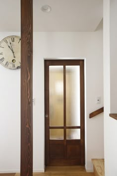 a clock on the wall above a wooden door in a room with white walls and wood flooring