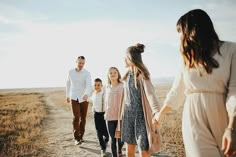 a family walking down a dirt road in the middle of an open field holding hands