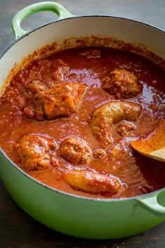 a green pot filled with meatballs and sauce on top of a wooden table next to a spoon