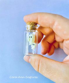 a hand holding a tiny glass bottle with a ghost in it's mouth on a blue background