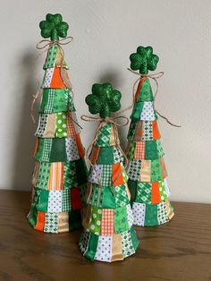 three small green and orange christmas trees with shamrocks on top, sitting on a wooden table