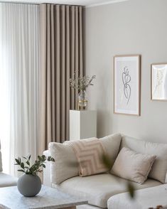 a living room with white couches and paintings on the wall above them, along with a coffee table