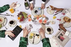 several people sitting around a table with plates and cups on it, all holding their hands together