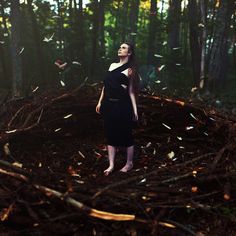 a woman standing in the middle of a forest surrounded by branches and birds flying around her