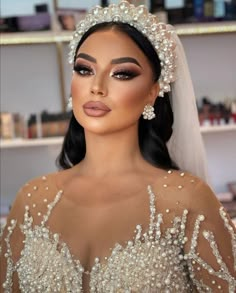 a woman wearing a bridal gown and veil with pearls on her head is looking at the camera