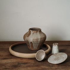 a brown and white vase sitting on top of a wooden table next to two cups