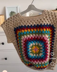 a crocheted sweater hanging on a clothes hanger in a room with white drawers