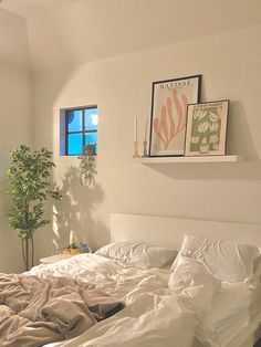 an unmade bed with white sheets and pillows in a bedroom next to a window