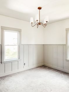 an empty room with two windows and a chandelier hanging from the light fixture